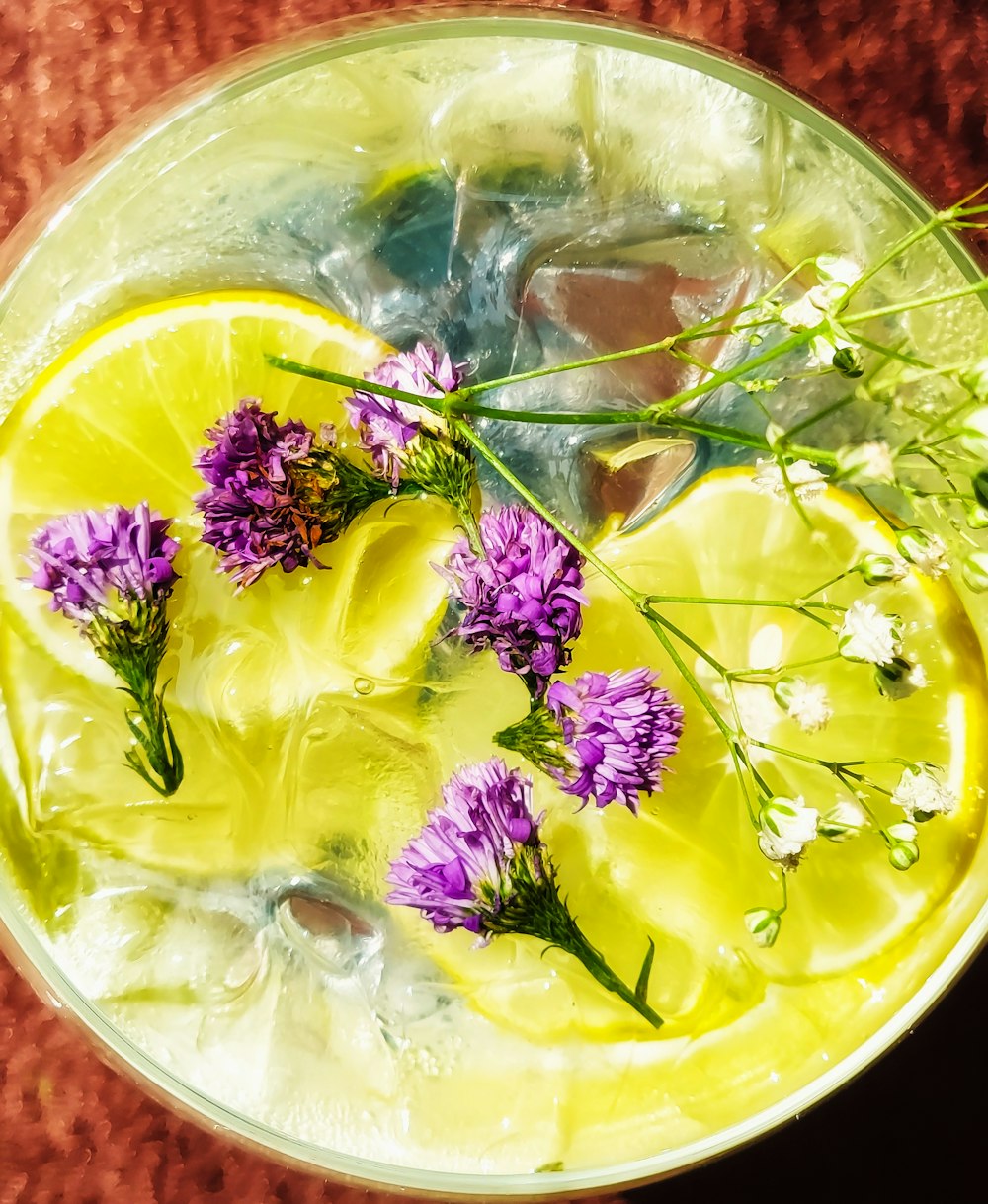 a glass of water with ice, lemon, and flowers