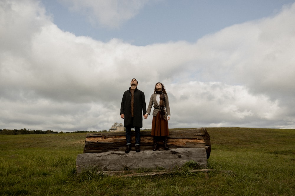 a man and a woman standing on a log in a field