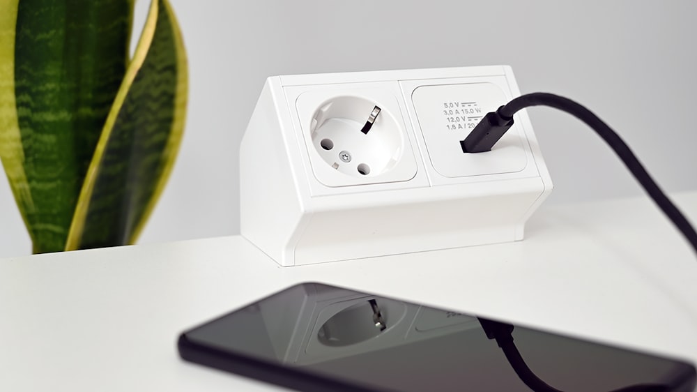 a phone charging on a white table next to a plant