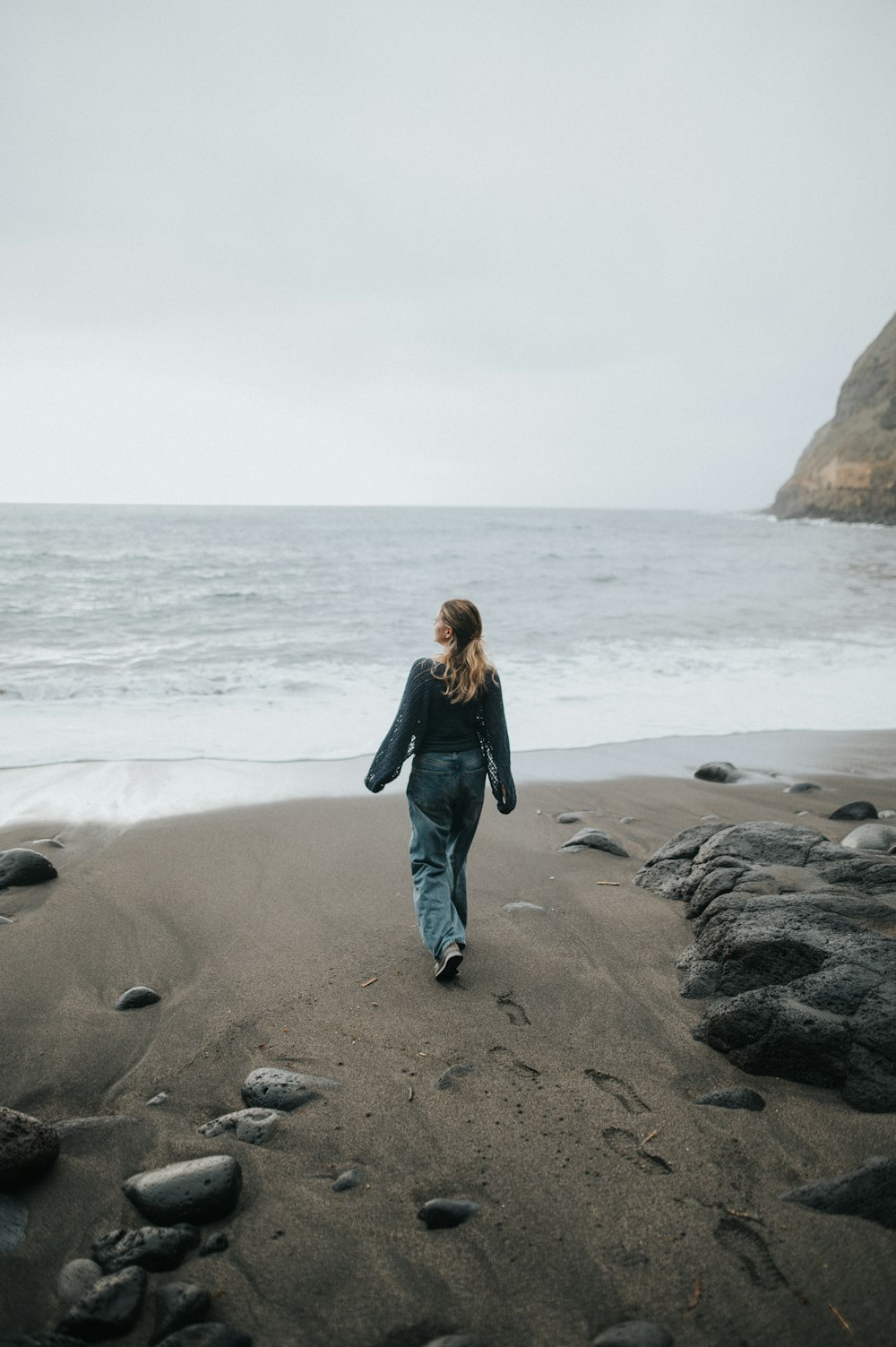 a woman walking along a beach next to the ocean