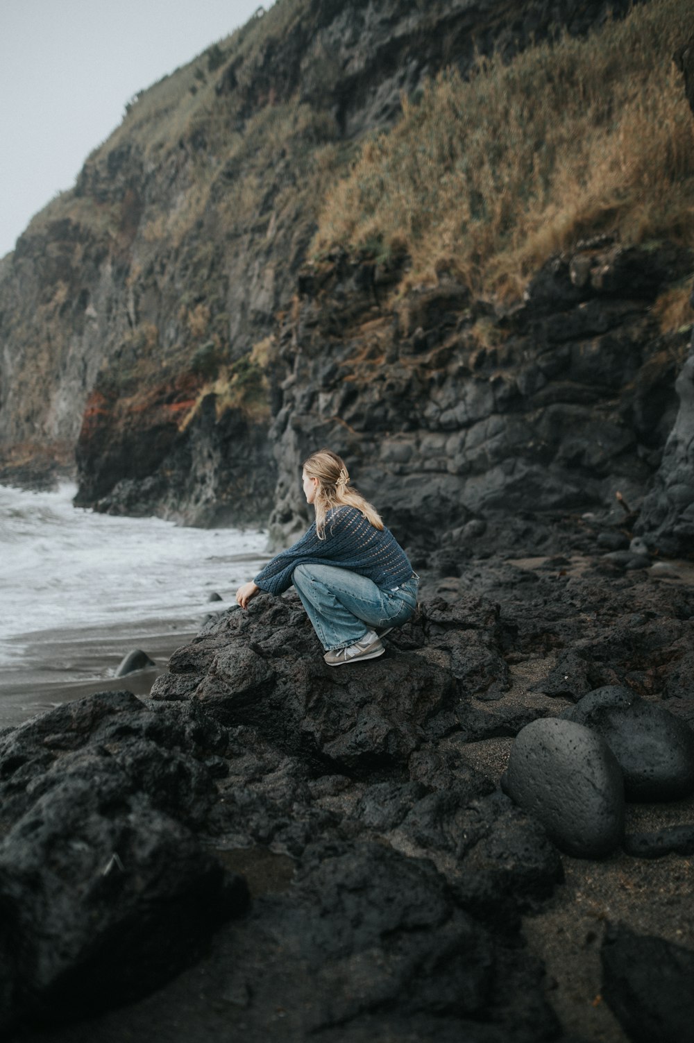 a woman sitting on a rock near the ocean