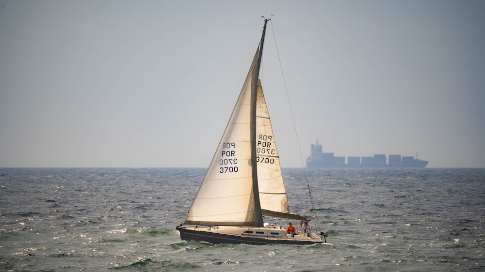 a sailboat sailing in the ocean with a cargo ship in the background