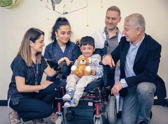 a group of people standing around a baby in a wheel chair