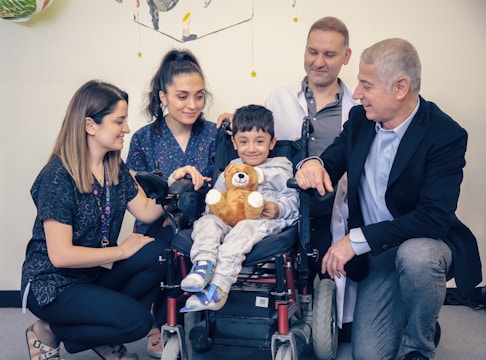a group of people standing around a baby in a wheel chair