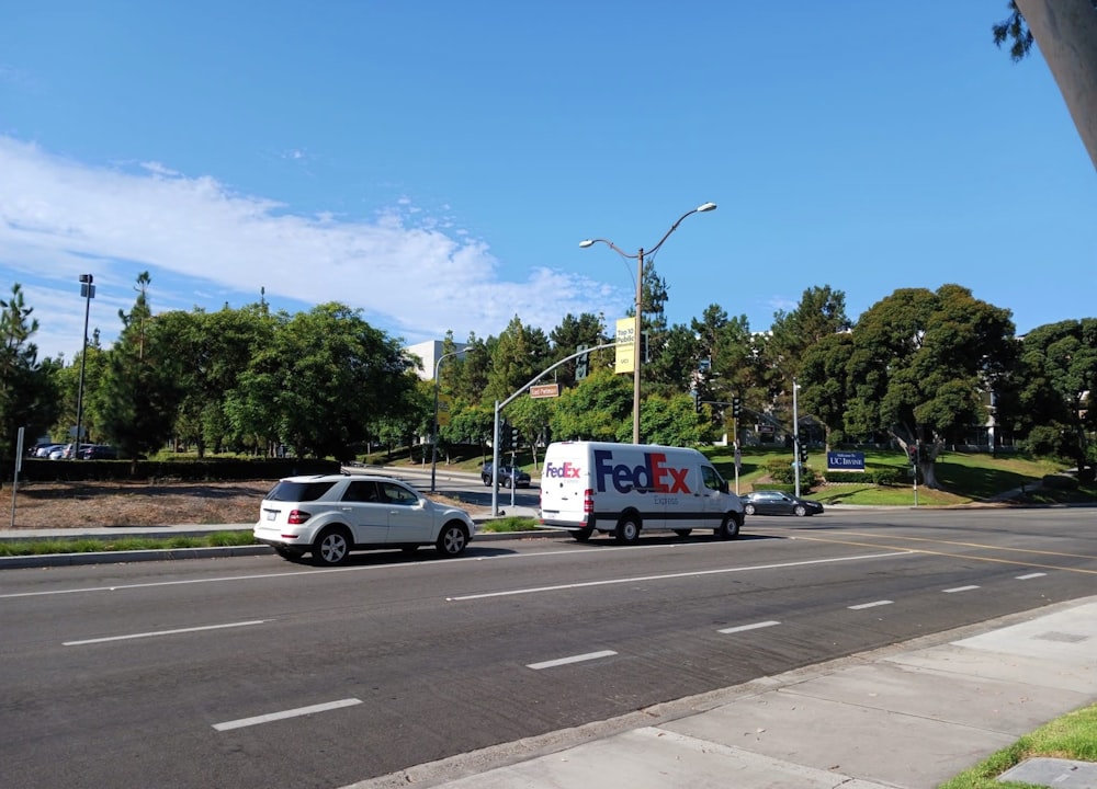 a fedex truck driving down a street next to a white van
