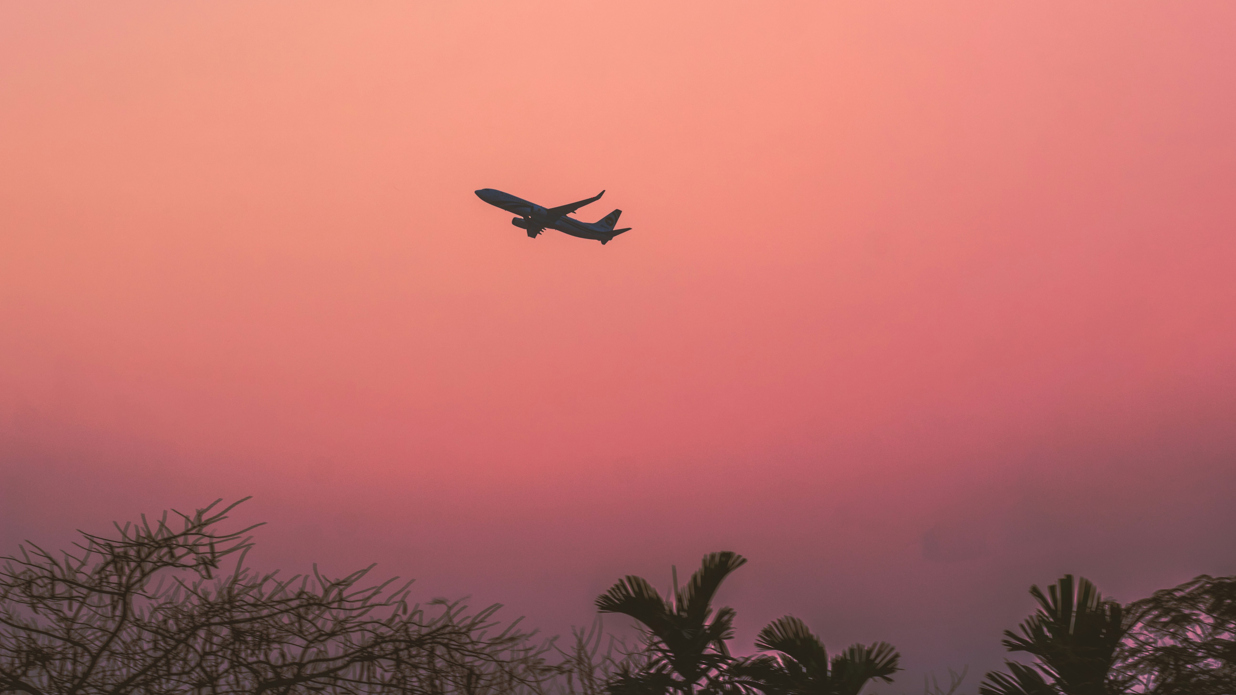 Avión despegando al atardecer con cielo naranja y rosa, nubes doradas en horizonte, perspectiva desde pista