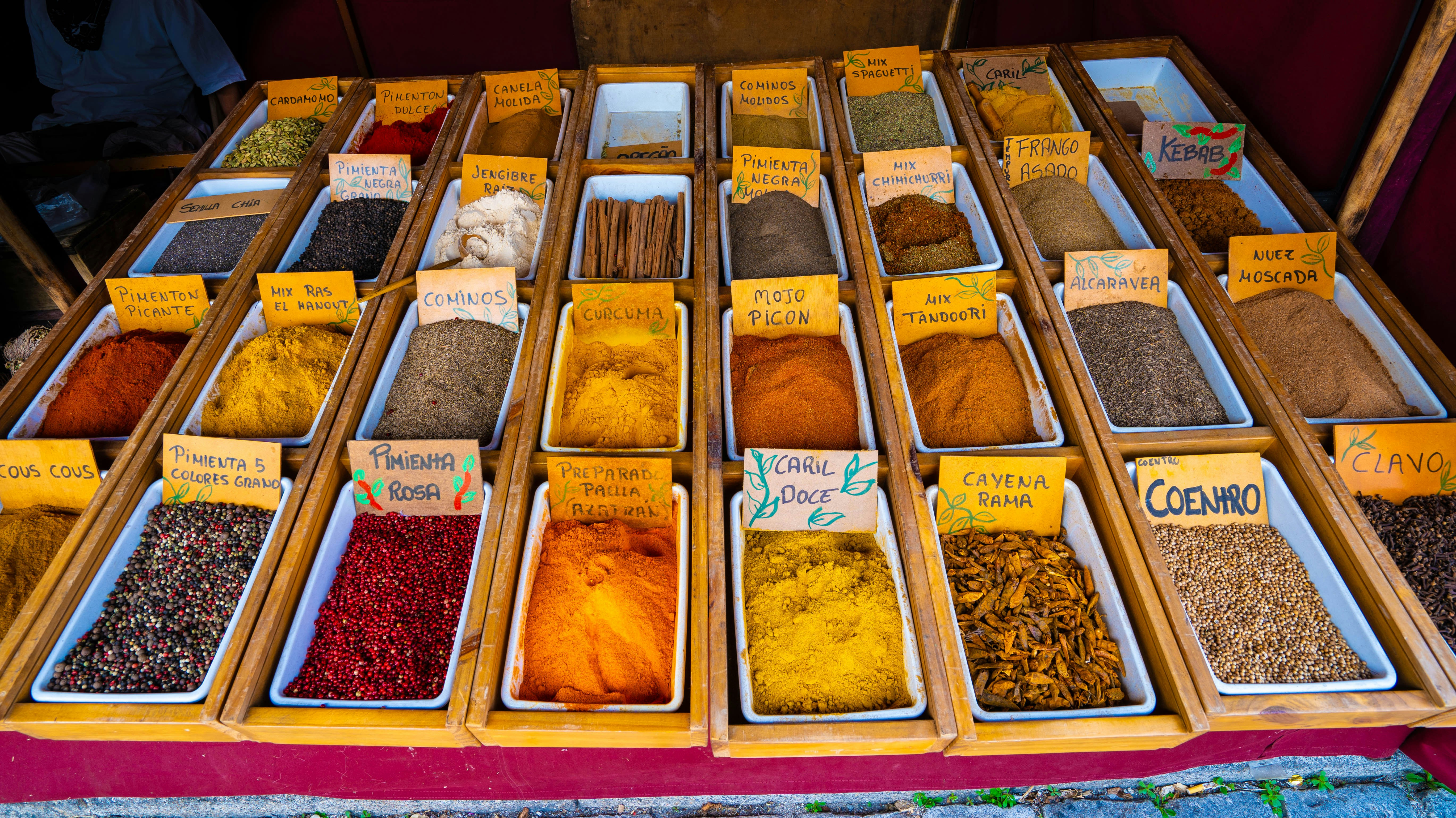 a variety of spices on display in wooden trays, Feast your eyes on the rich tapestry of spices from around the world! This colorful array beckons with aromatic promises, offering a zestful journey for the senses. Whether you