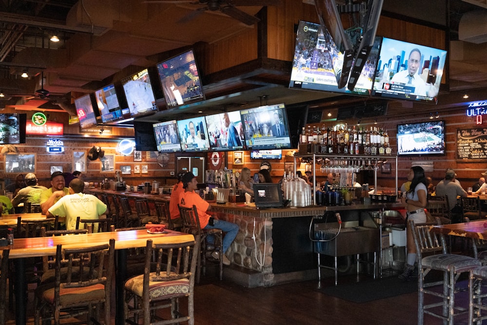 a group of people sitting at a bar watching tvs