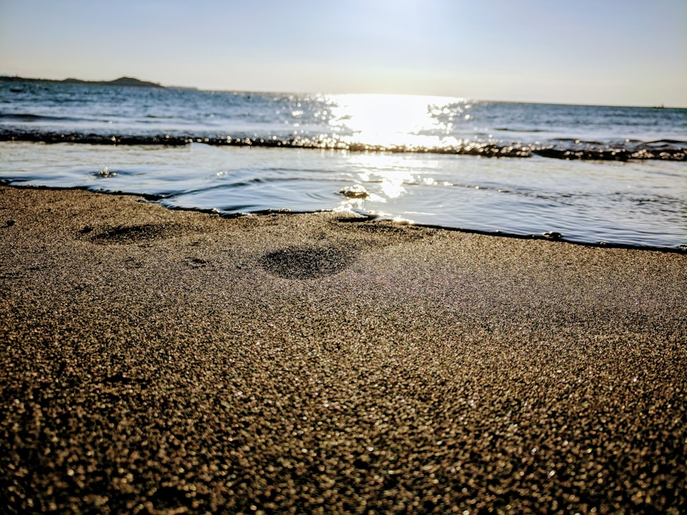 a sandy beach next to the ocean under a blue sky