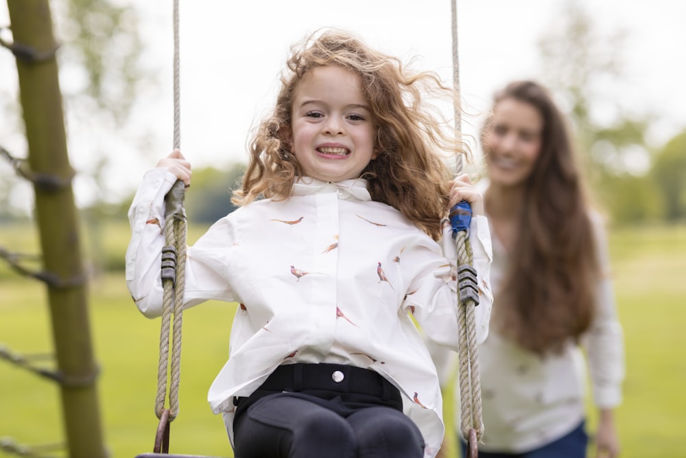 a young girl sitting on a swing next to a woman