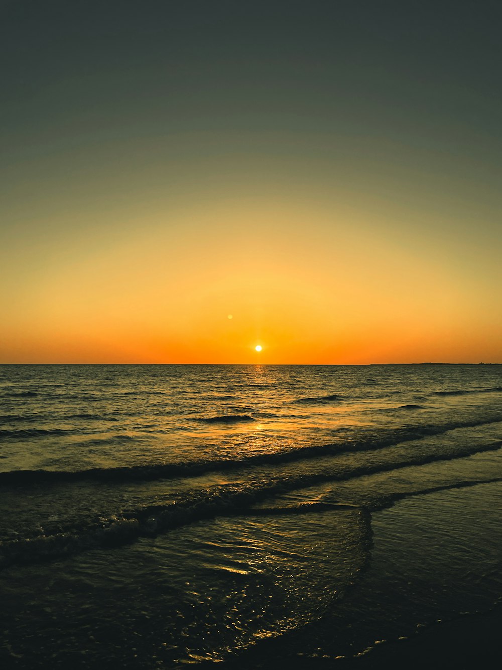 the sun is setting over the water at the beach