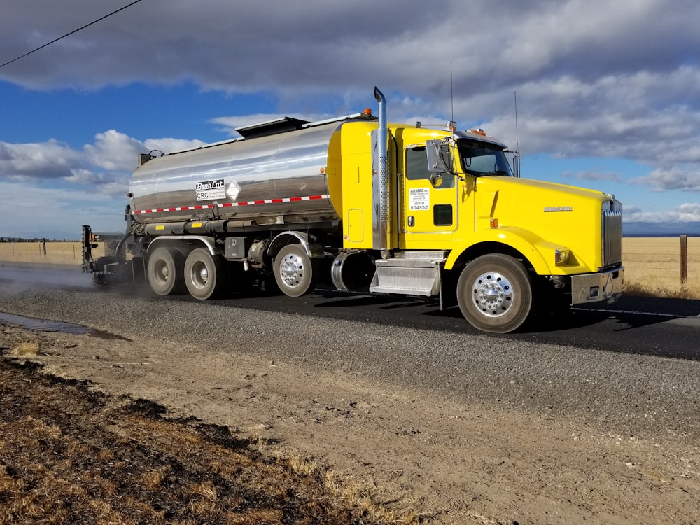 a yellow tanker truck driving down a rural road
