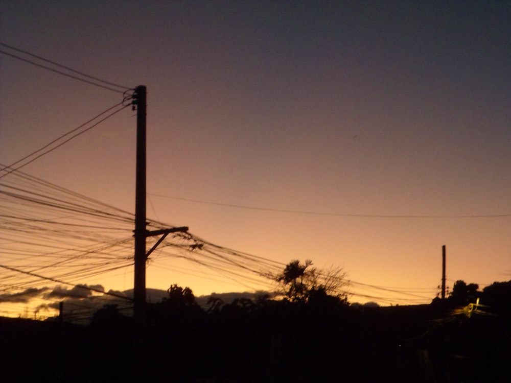 the sun is setting behind power lines and telephone poles