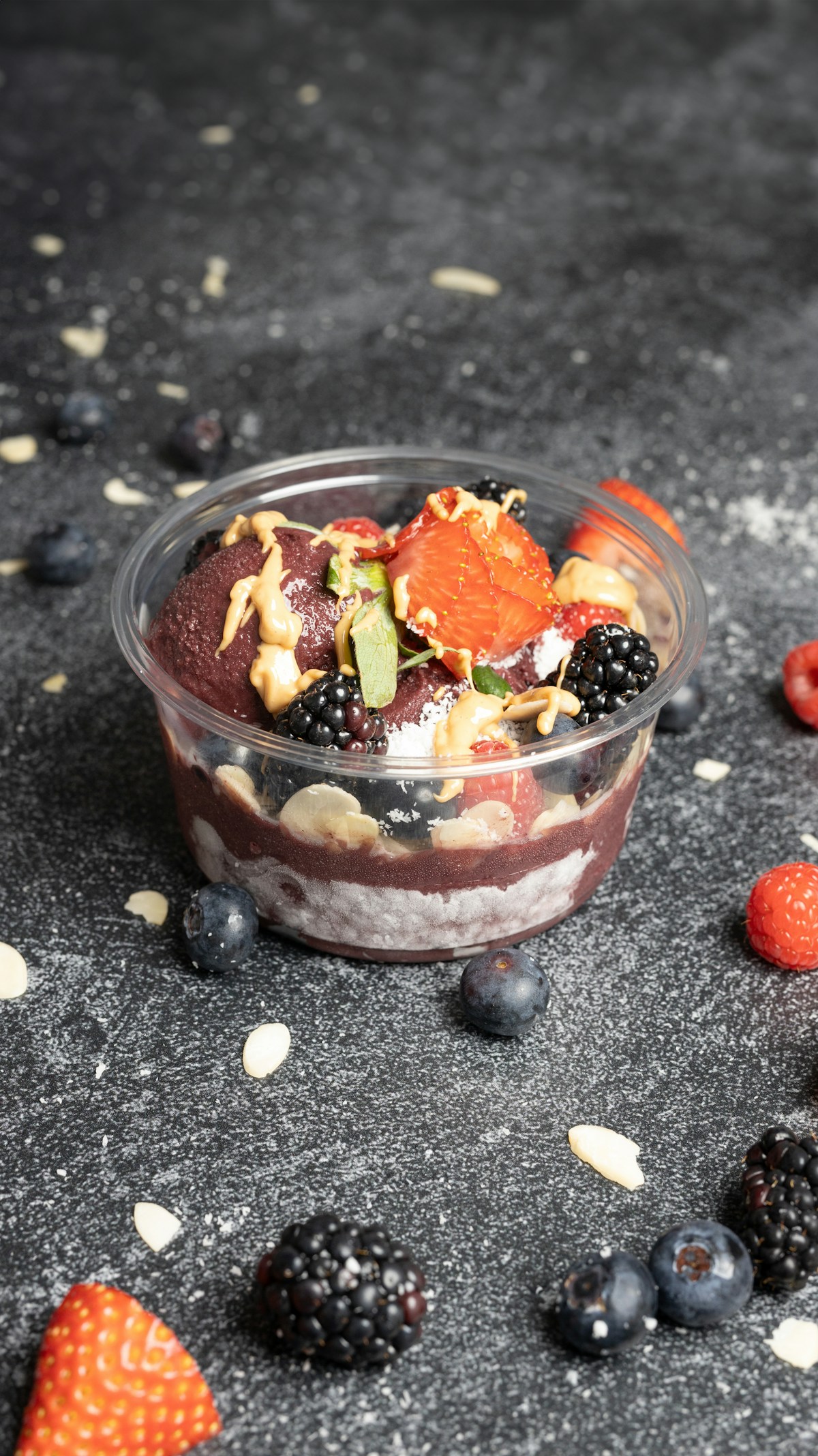 Copo de açaí com frutas vermelhas, banana e calda por cima