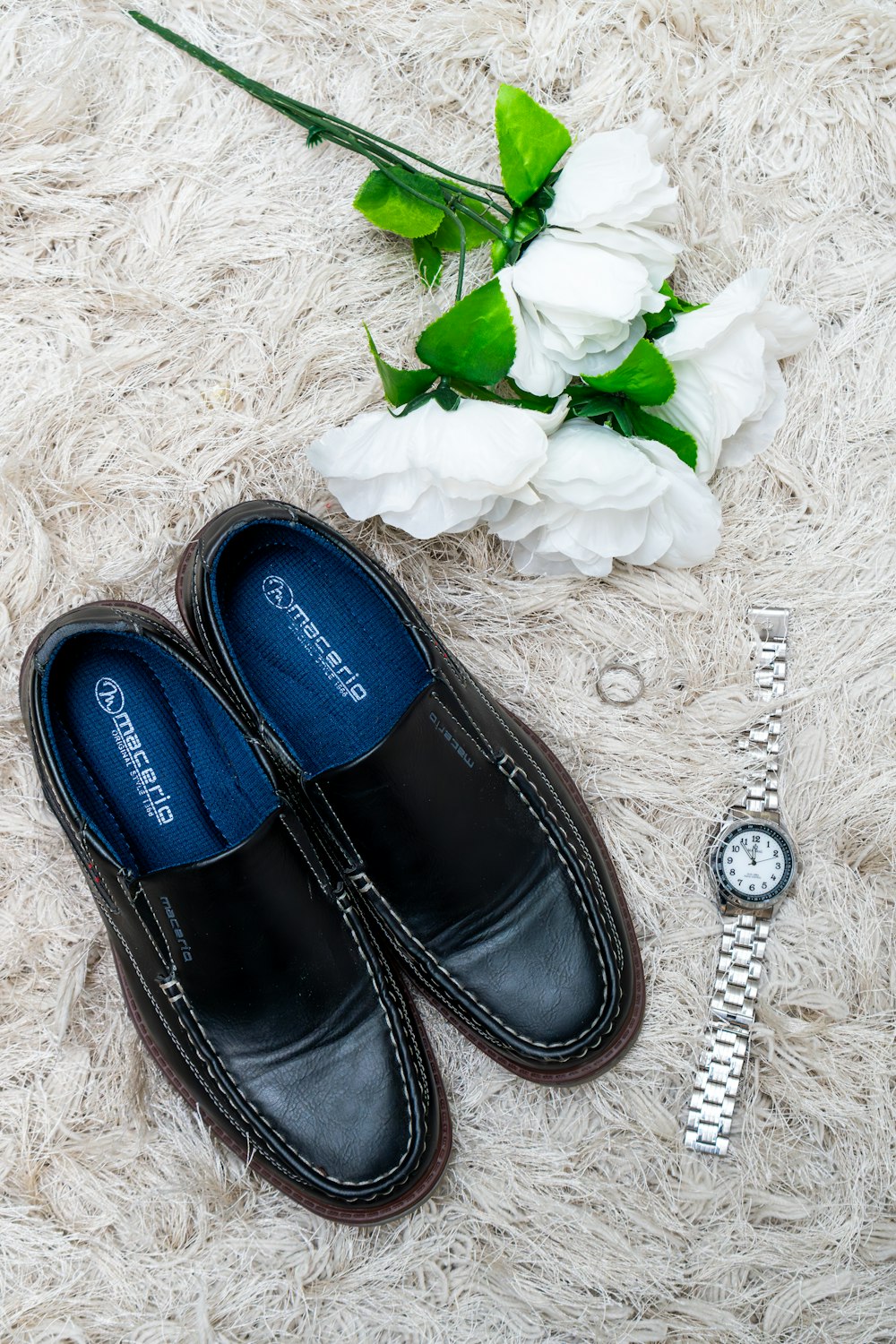 a pair of black shoes sitting on top of a white rug next to a watch