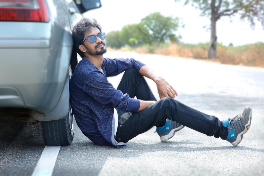 a man sitting on the side of a road next to a car