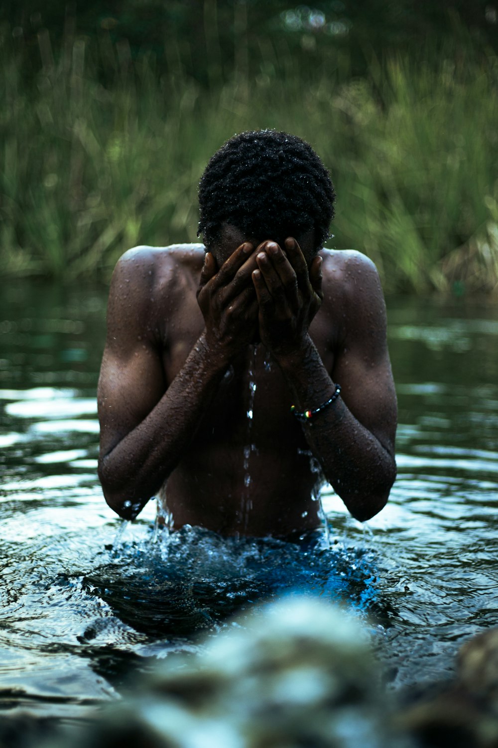 a man standing in a body of water covering his face with his hands