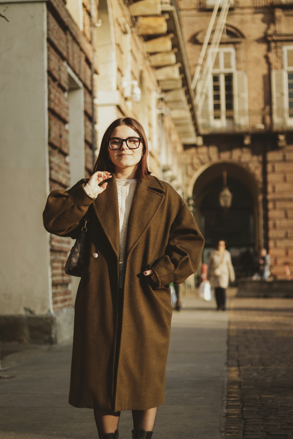 a woman in a brown coat is standing on a sidewalk
