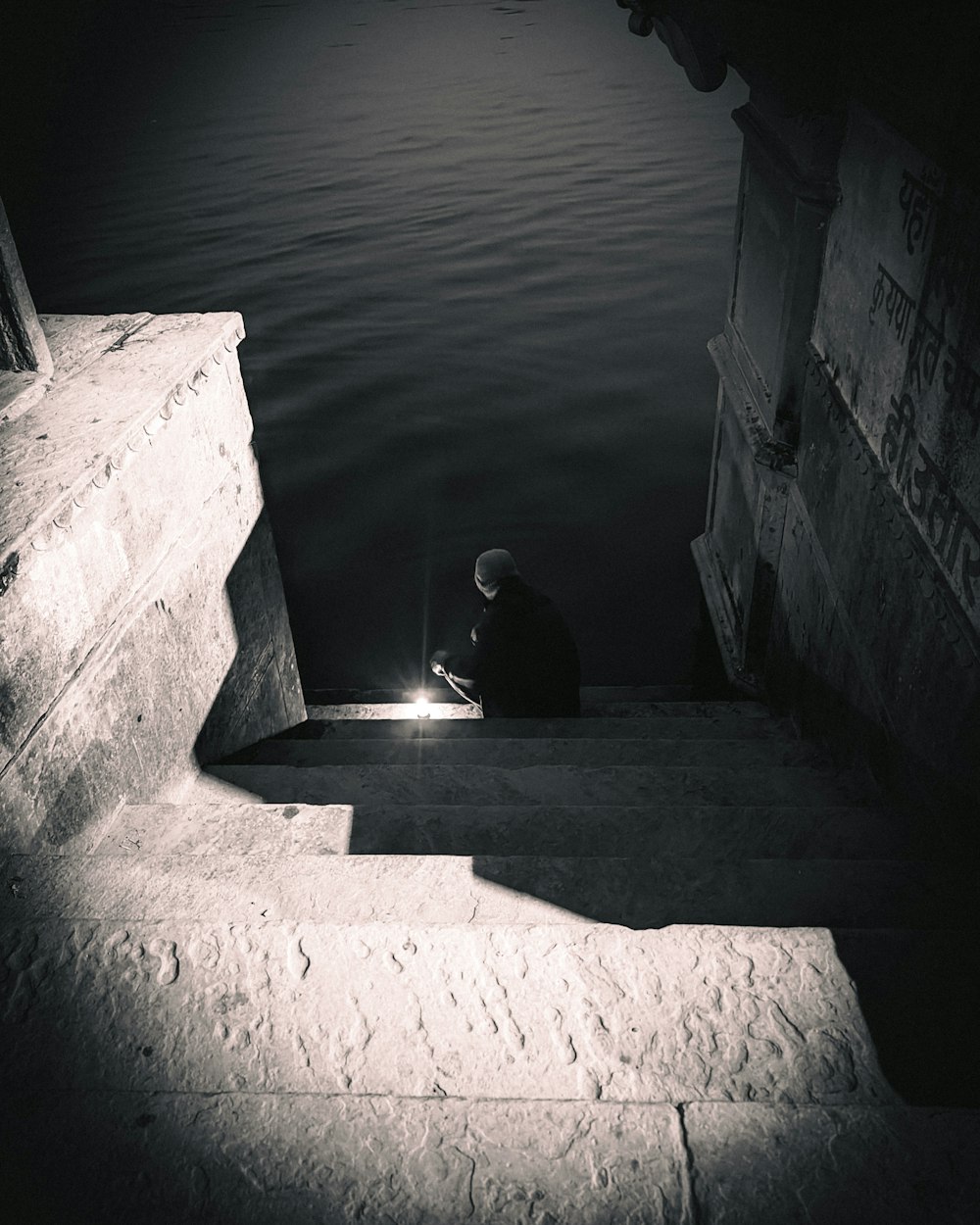 uma pessoa sentada em um conjunto de escadas ao lado de um corpo de água