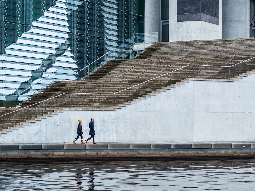 a couple of people walking down a sidewalk next to a body of water
