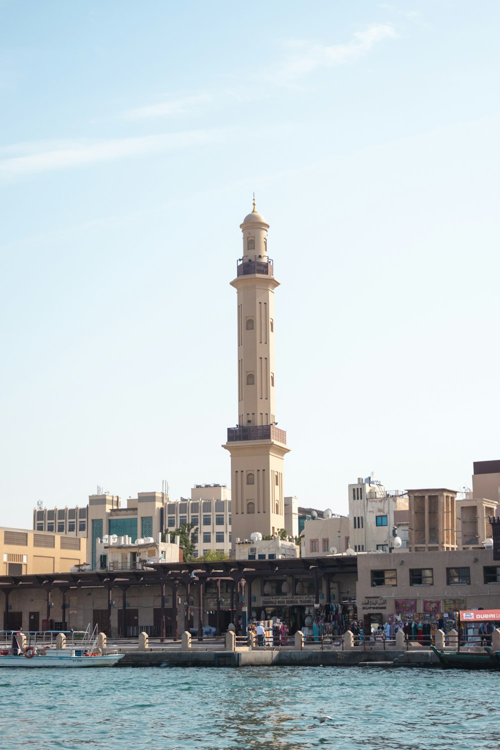 uma alta torre do relógio elevando-se sobre uma cidade ao lado de um corpo de água