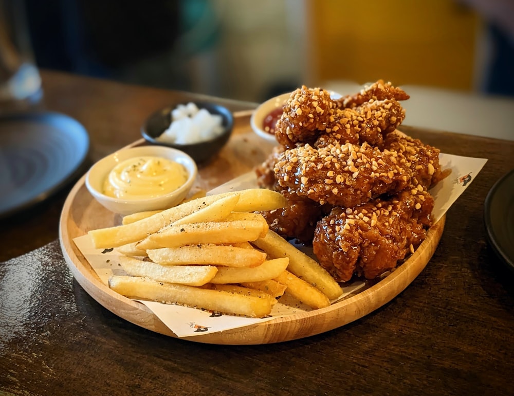 a wooden plate topped with fried chicken and french fries