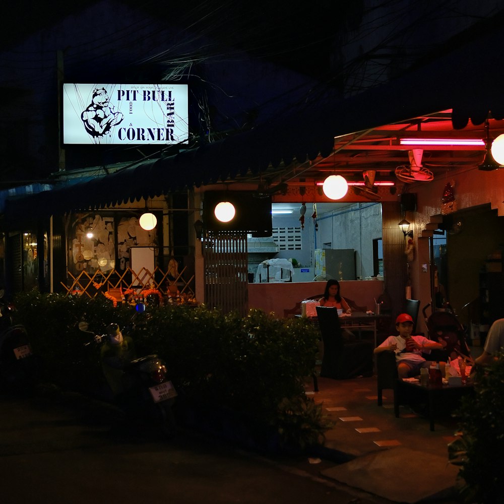 a group of people sitting outside of a restaurant at night