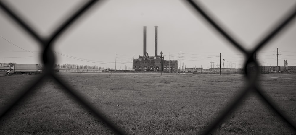 a black and white photo of a factory behind a fence