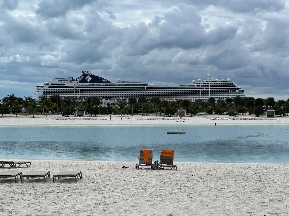 two lounge chairs on a beach with a cruise ship in the background