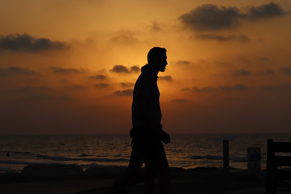 a man walking on the beach at sunset