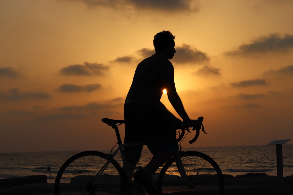 a man riding a bike on a beach at sunset