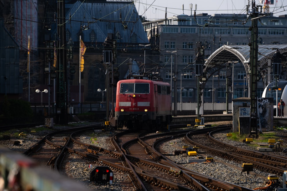 a red train traveling down train tracks next to tall buildings