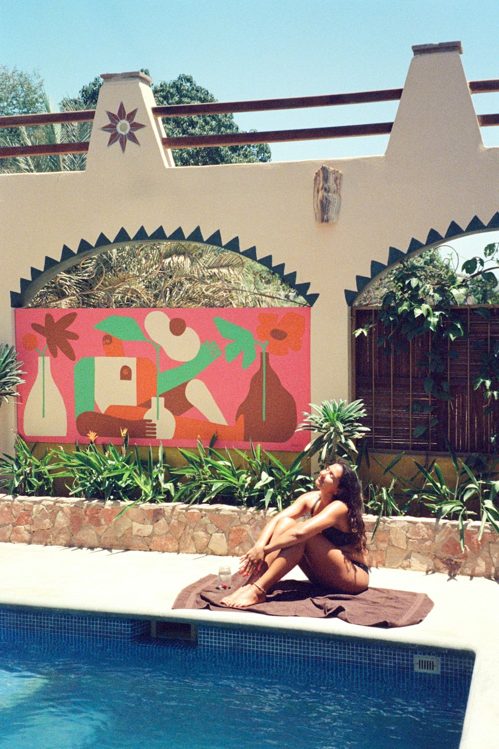 a woman sitting on a towel next to a swimming pool