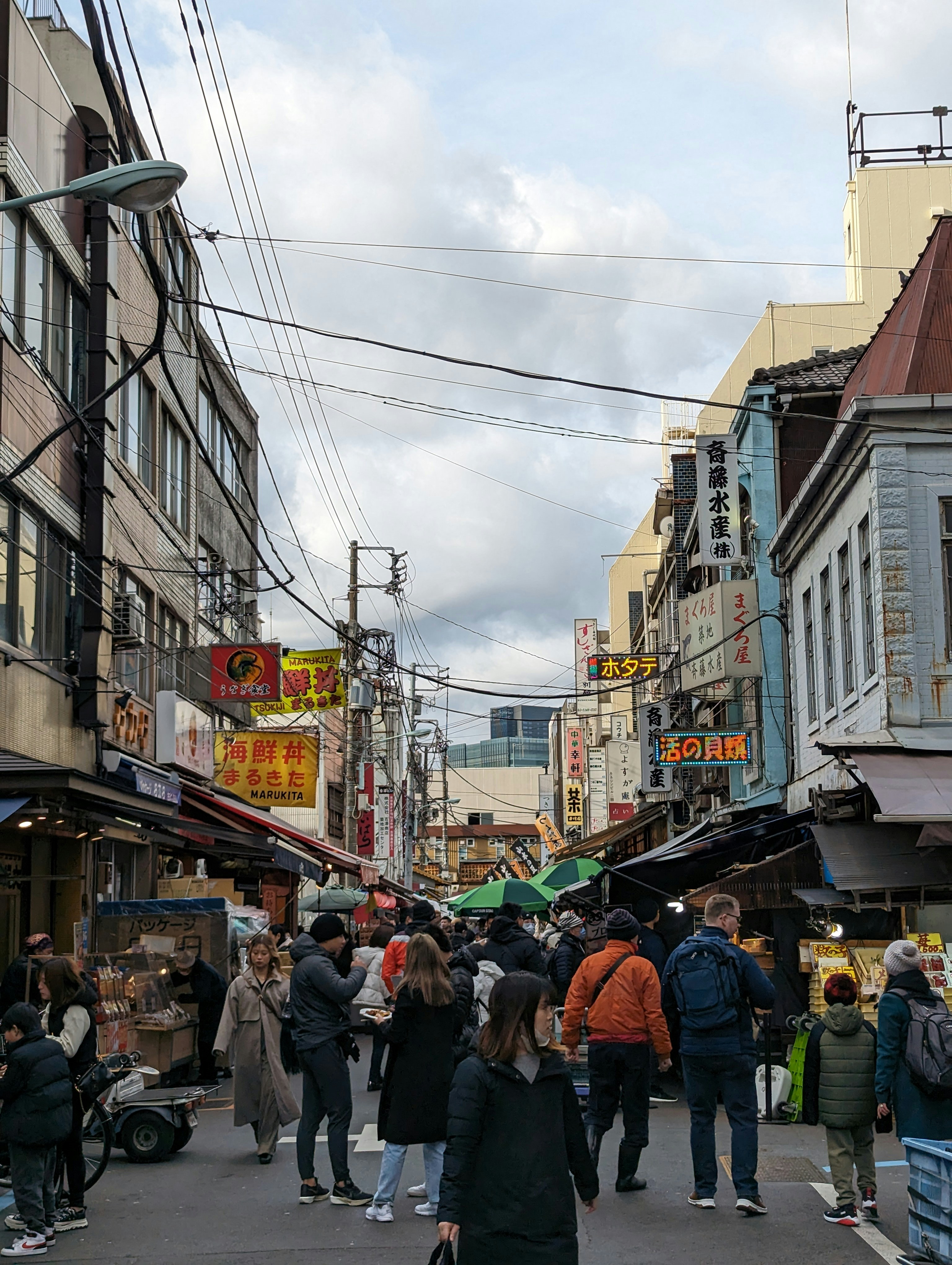 Crowd walking down a narrow Tsukiji Fish Market alley between tall buildings