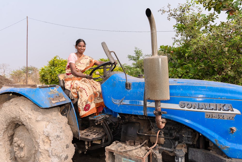 a woman sitting on the front of a blue tractor
