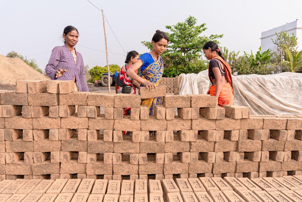 a group of women standing next to a pile of bricks