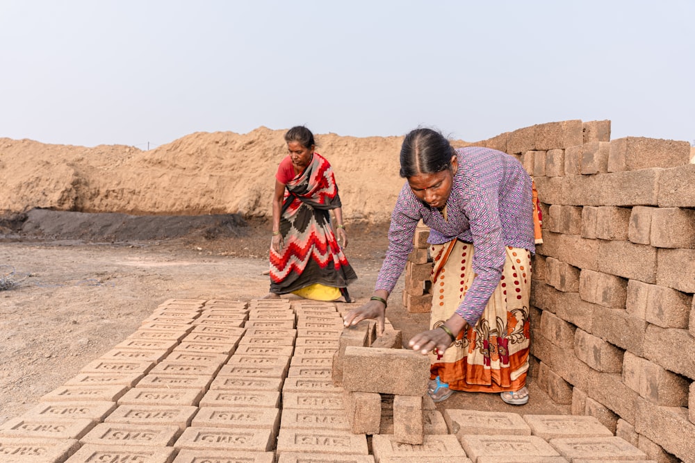 a couple of women standing next to a pile of bricks