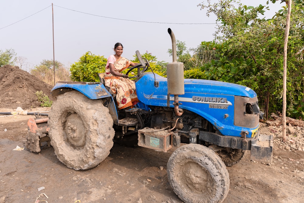 a woman riding on the back of a blue tractor