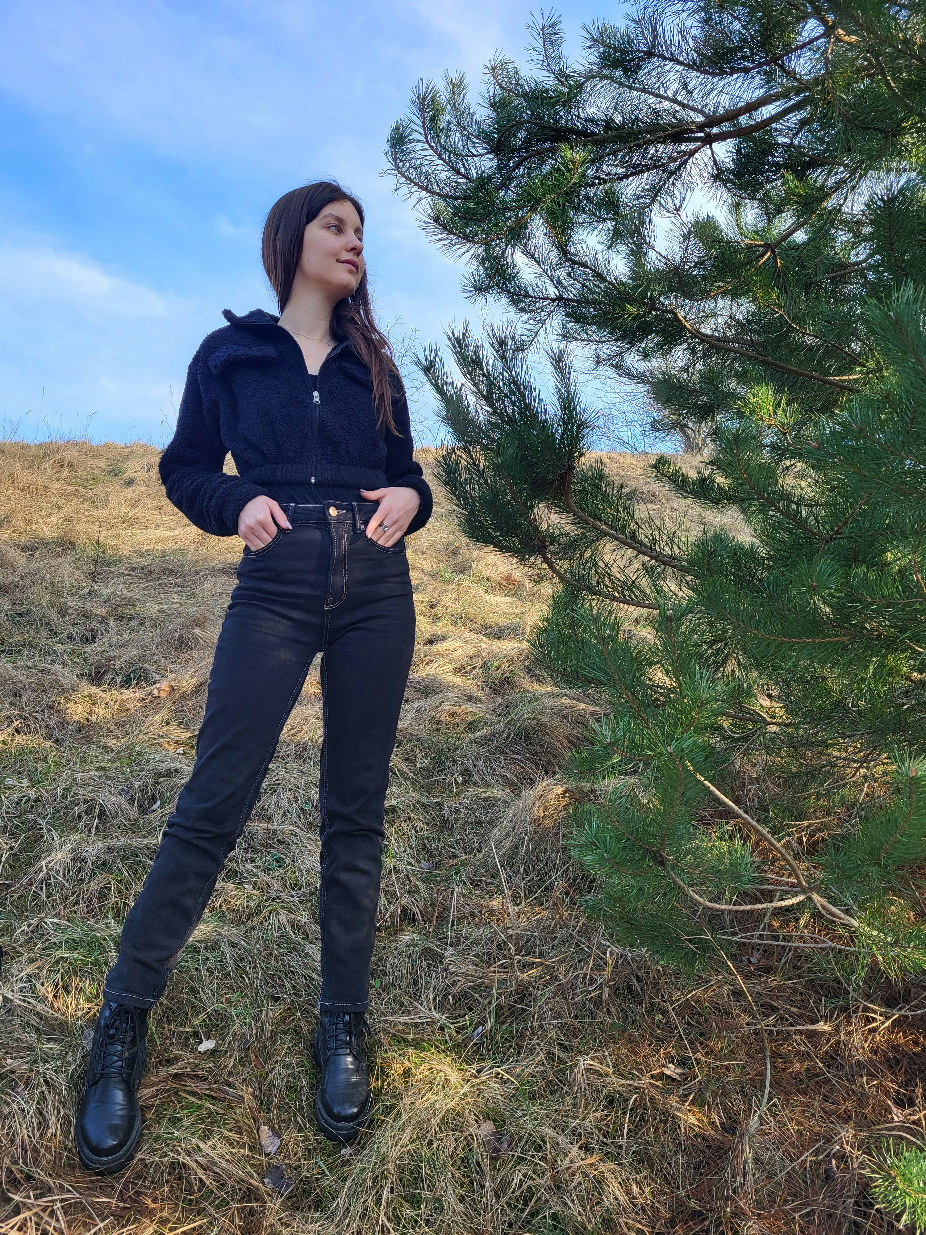 a woman standing in a field next to a pine tree