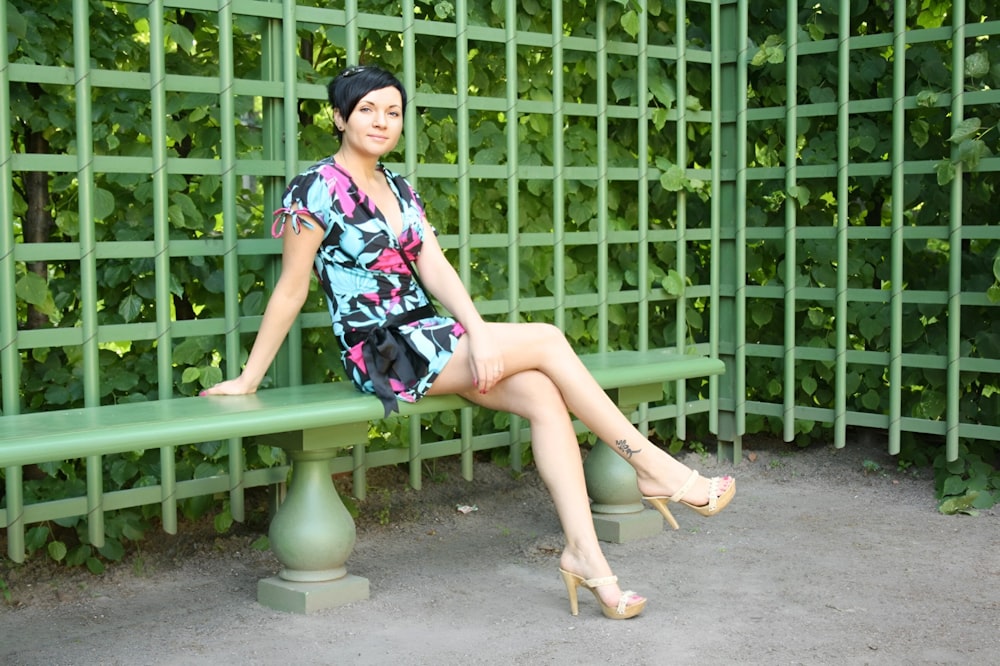 a woman sitting on a bench in front of a green fence