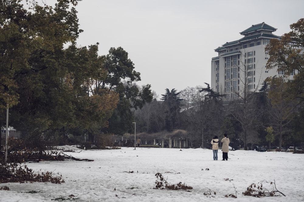 two people standing in the snow in front of a building