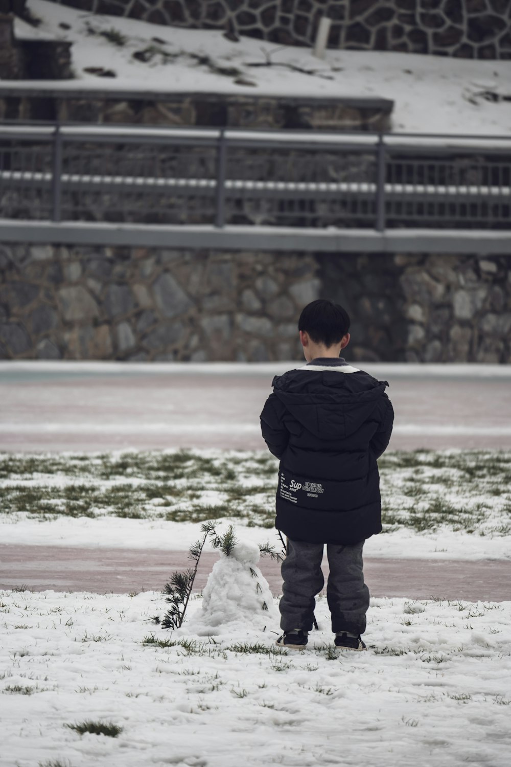 a young boy standing in the snow next to a snowboard