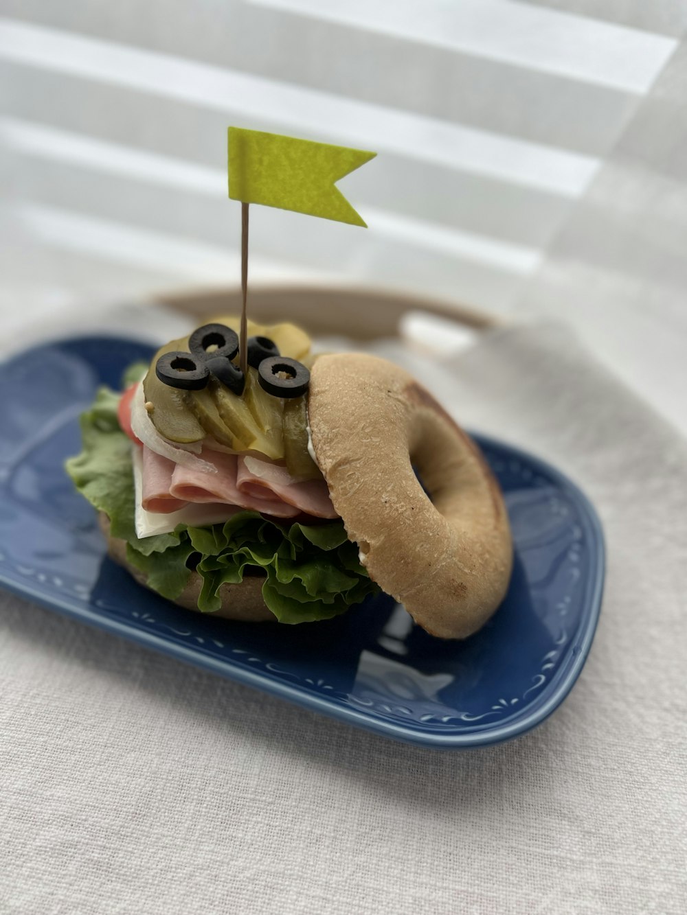 a sandwich with a bagel and olives on a blue plate