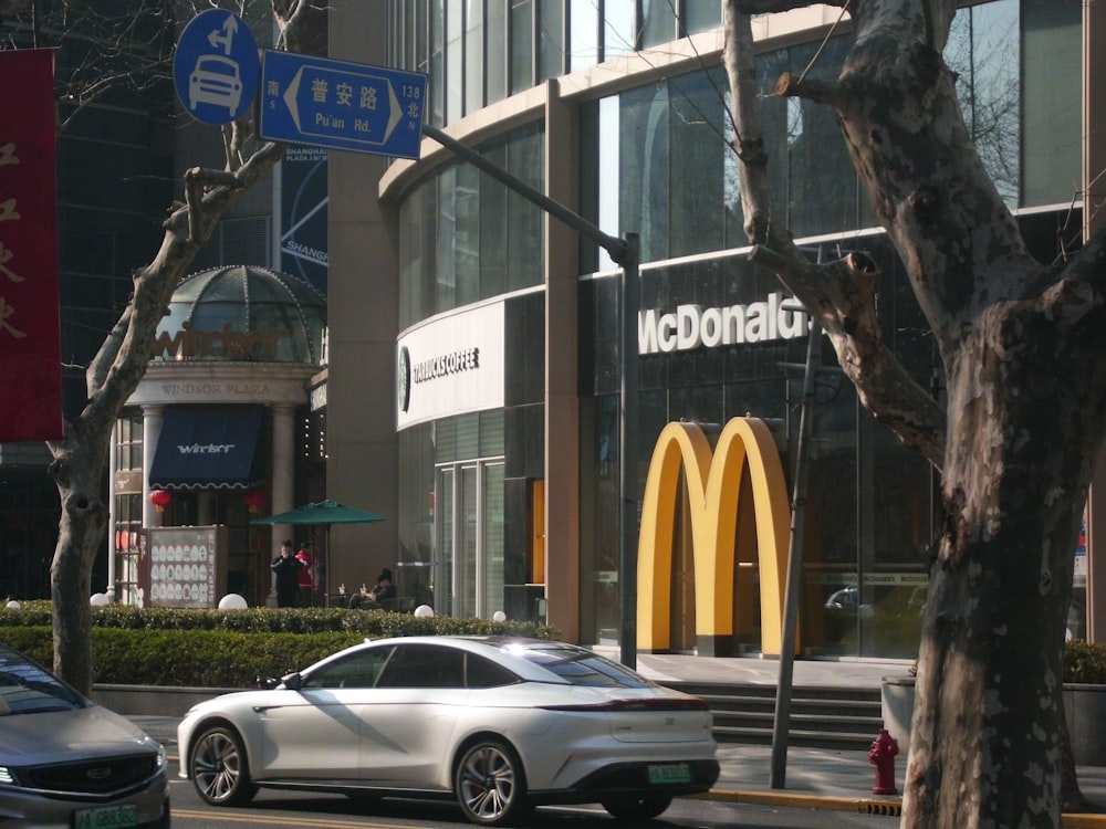 a white car driving down a street next to a mcdonald's