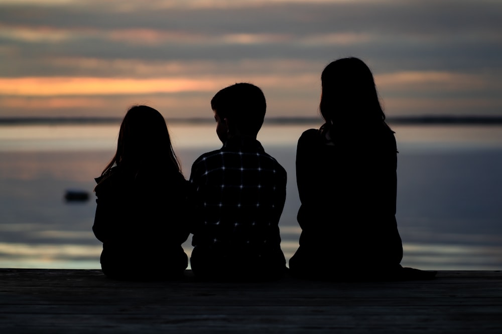 three people sitting on a dock watching the sunset