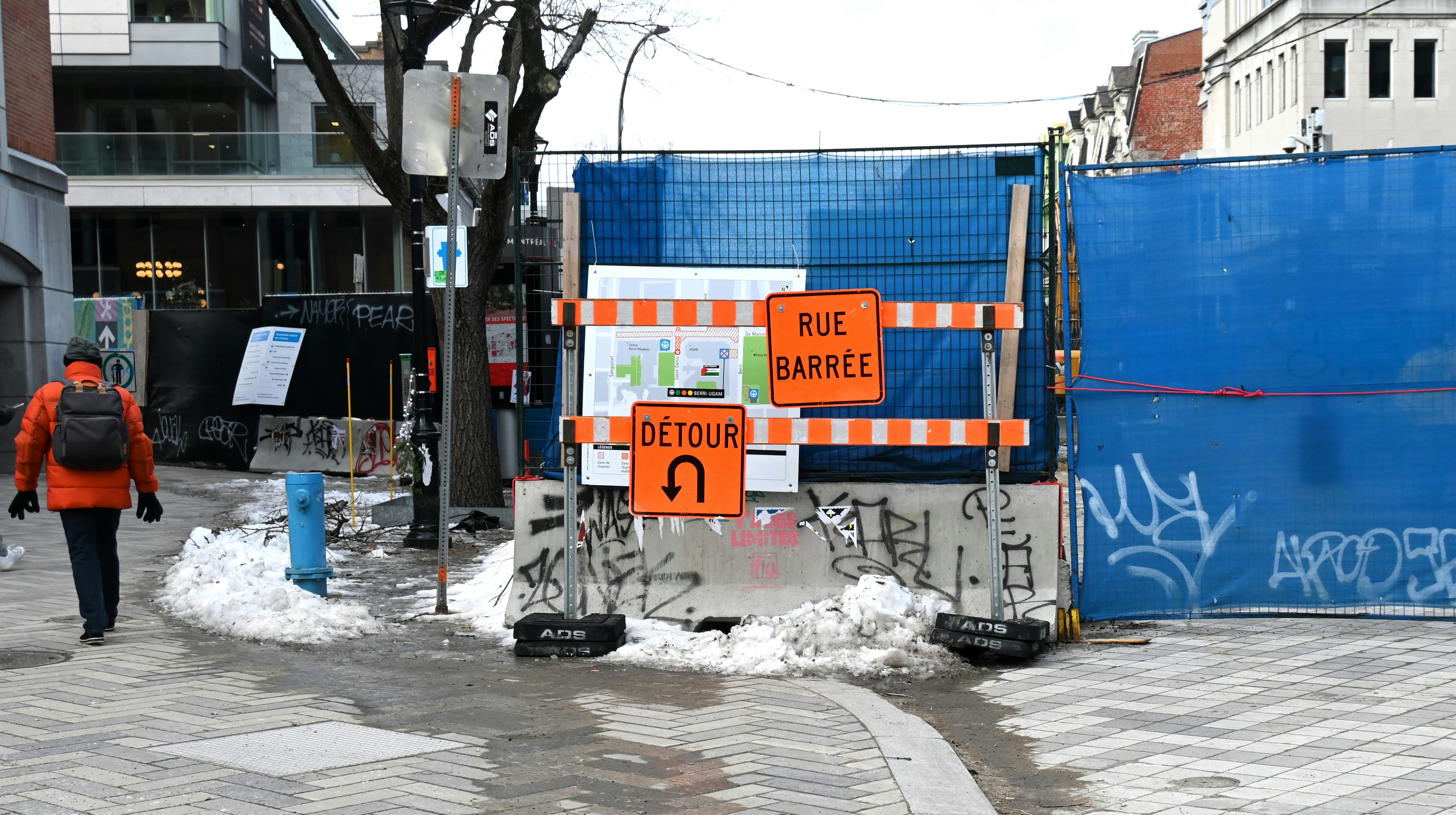 Un hombre caminando por una calle junto a una valla azul