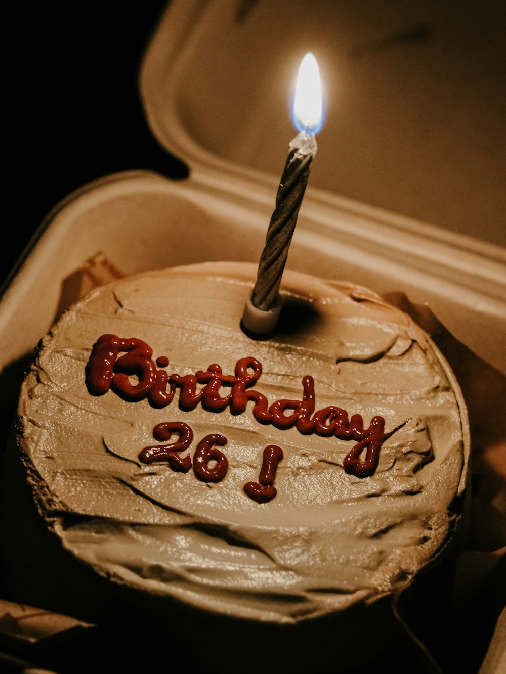 a birthday cake with a lit candle in a box