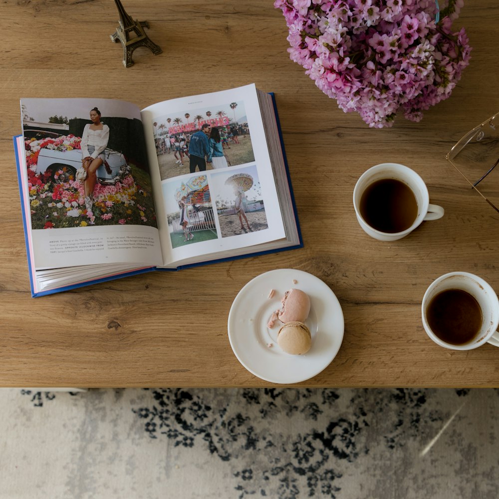 a table topped with two cups of coffee and a book