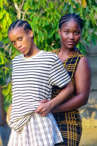 two women standing next to each other in front of a tree