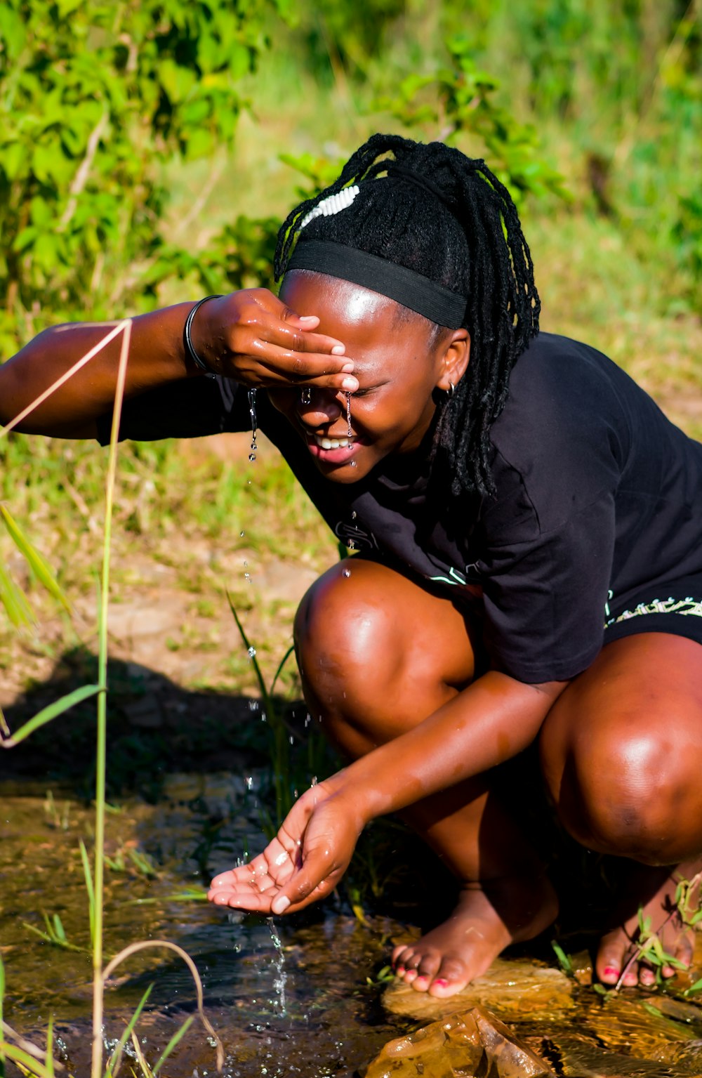 a woman crouches down to collect water from a stream